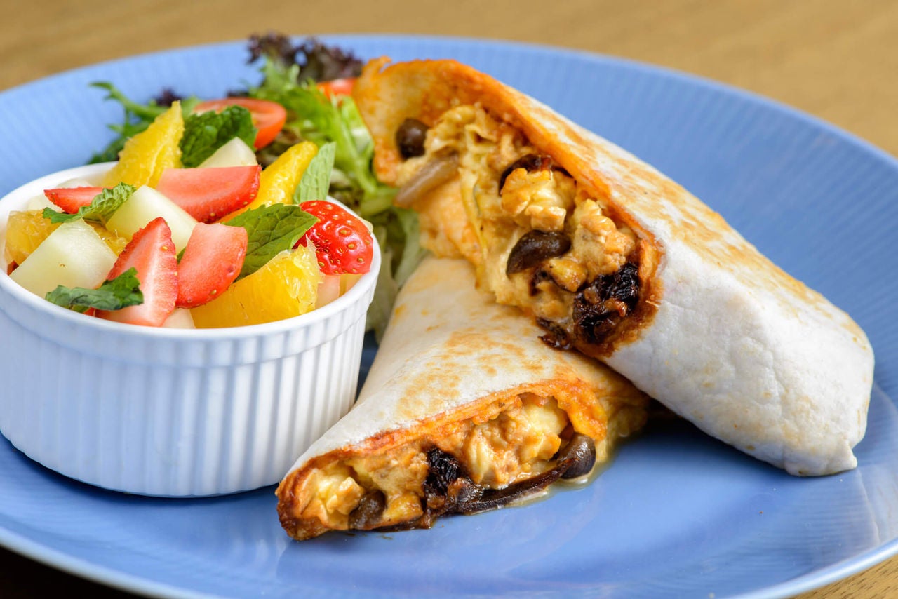 Wrap with beans and eggs on a plate with a side of fruit salad.