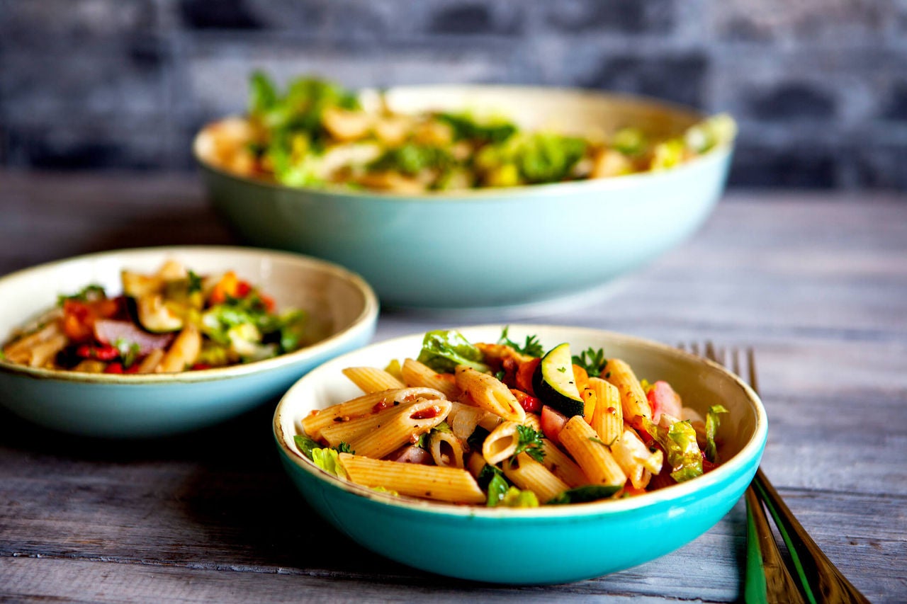 Bowls of penne pasta with chopped vegetables and herbs.