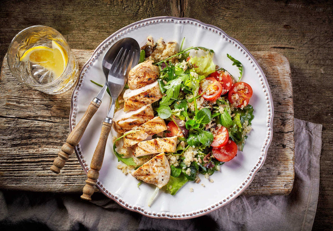 Salad with grilled chicken, quinoa, tomatoes and a glass with lemons on the side.