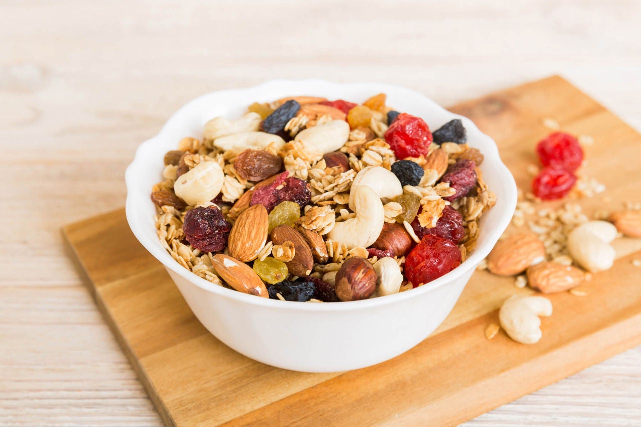 Bowl of trail mix with almonds, cashews, dried fruit and oats.