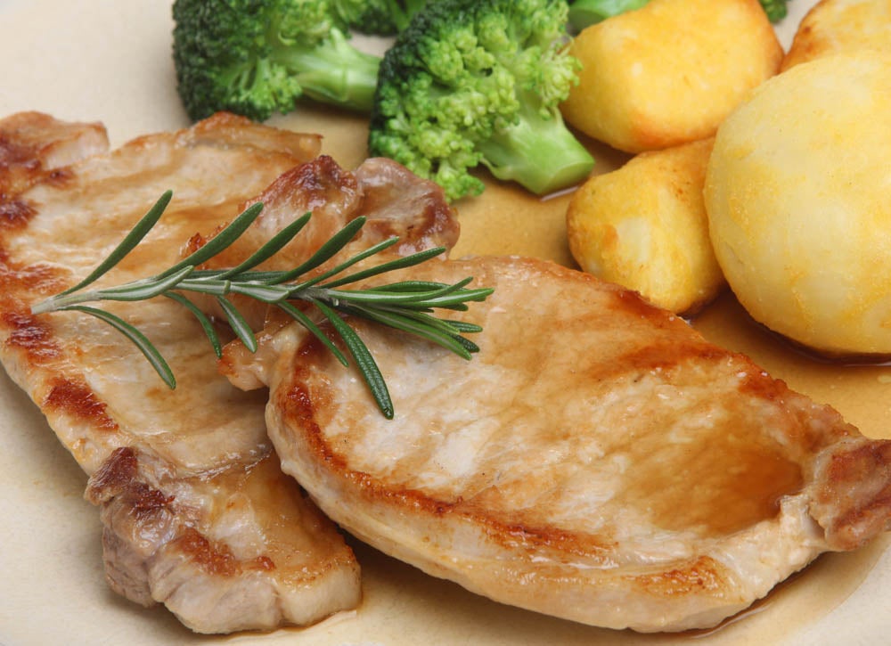 Grilled pork chops served with roasted potatoes and broccoli, garnished with a rosemary sprig.