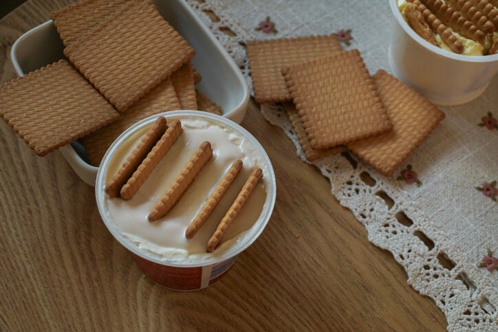 Tub of cheesecake mix with cookies dipped into, next to a bowl of cookies.