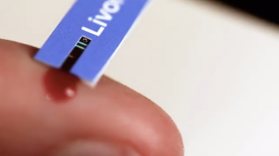 Close-up of a blood glucose test strip collecting a drop of blood from a fingertip.
