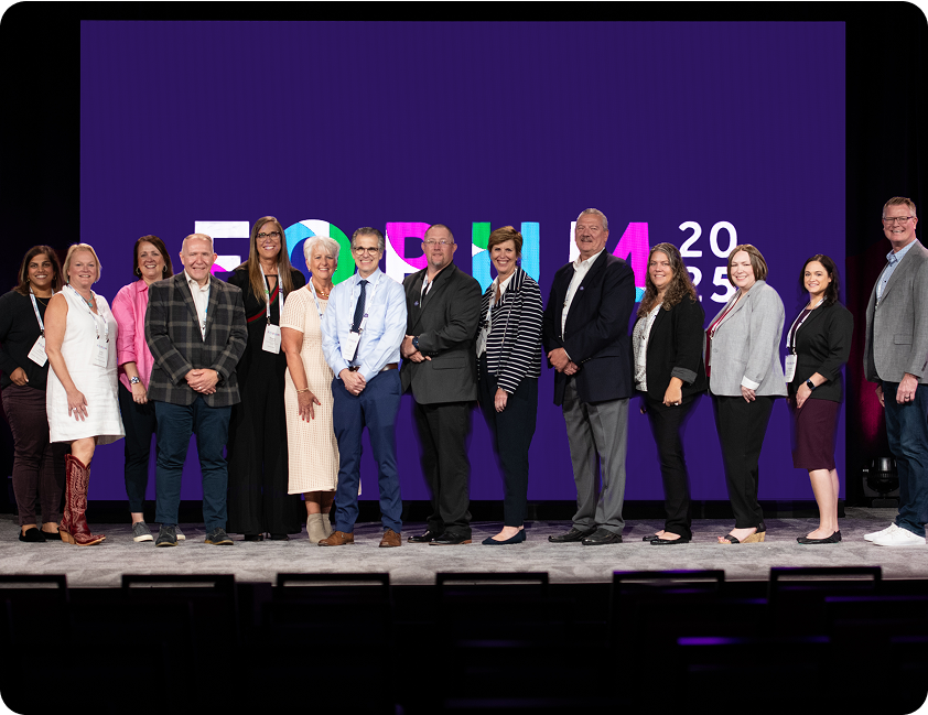 A group of attendees at the Forum 2025 event. They are posing in front of a Forum 2025 banner.