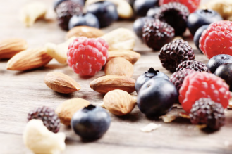  A close-up of a variety of nuts and berries, including almonds, blueberries, blackberries, and raspberries, scattered on a wooden surface.