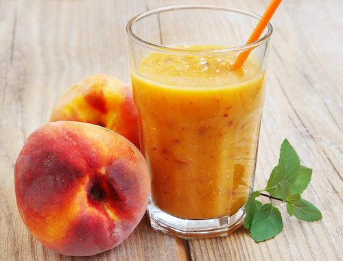 Peach Smoothie in Glass cup witn Orange Straw Next to Fresh Peaches