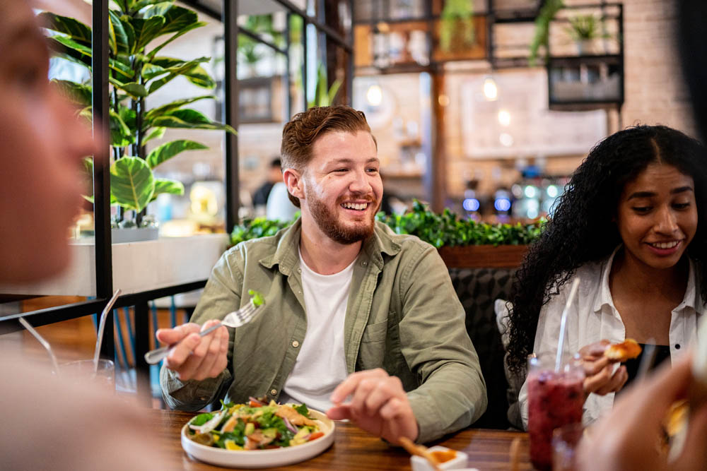 A group of friends enjoying a meal together at a restaurant, laughing and engaging in conversation over healthy food and drinks.