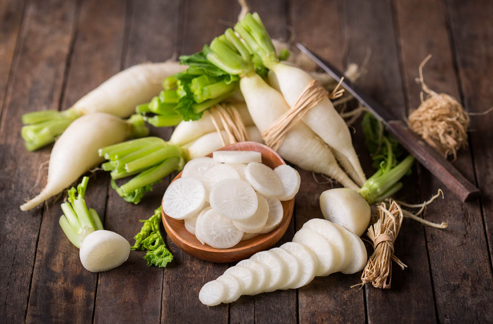 A collection of fresh, white radishes and radish tops on a wooden surface.