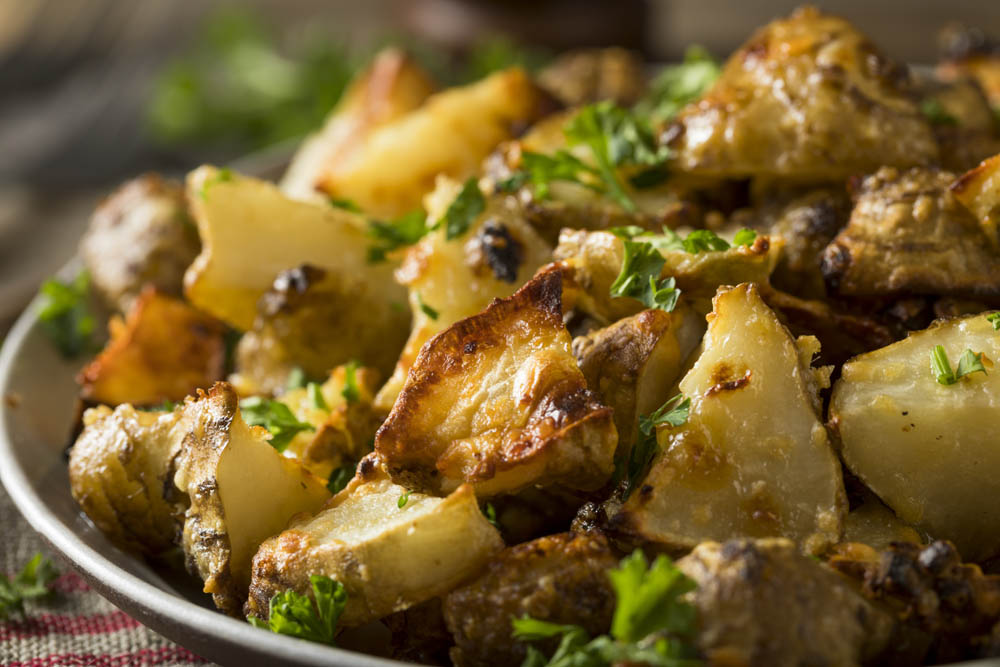 A close-up of golden, roasted potatoes garnished with chopped parsley in a serving dish.