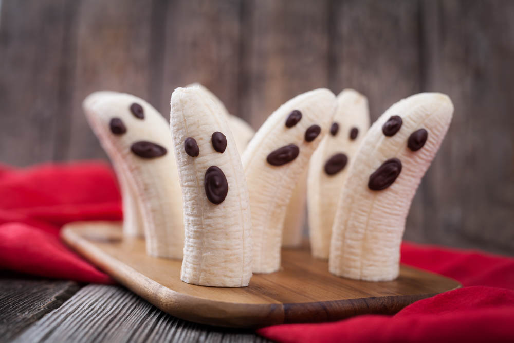Banana ghosts with chocolate faces arranged on a wooden tray, creating a fun and spooky Halloween-themed snack.