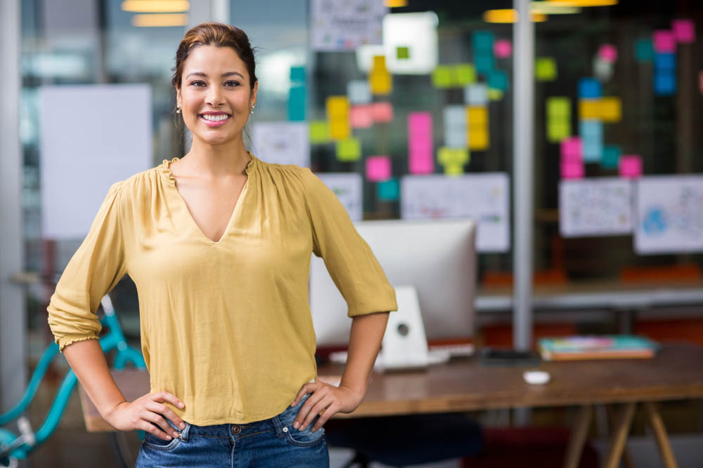 Confident woman standing in a modern office with sticky notes on the glass wall behind her.