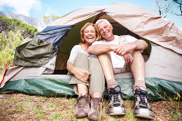 An older man and woman smiling together. They are sitting at the entryway of their tent.