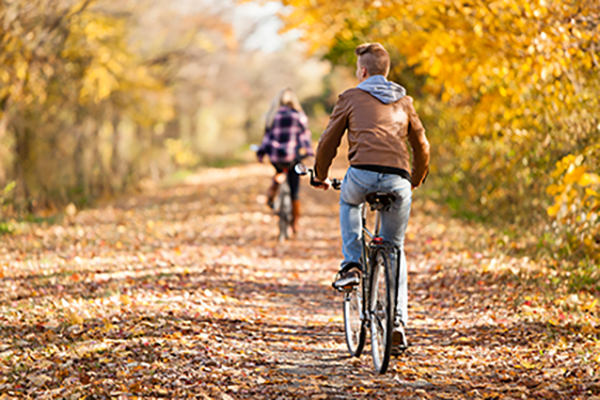 A man and a woman bicycling down a path of freshly fallen autumn leaves.