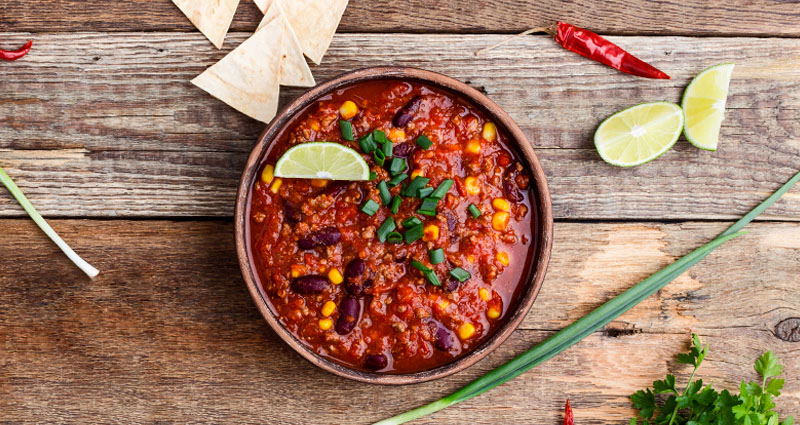 A bowl of healthy chili topped with green onions and lime with a side of tortilla chips.