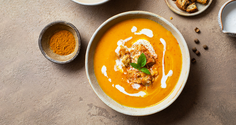 A bowl of butternut squash soup topped with ground cinnamon and cream.