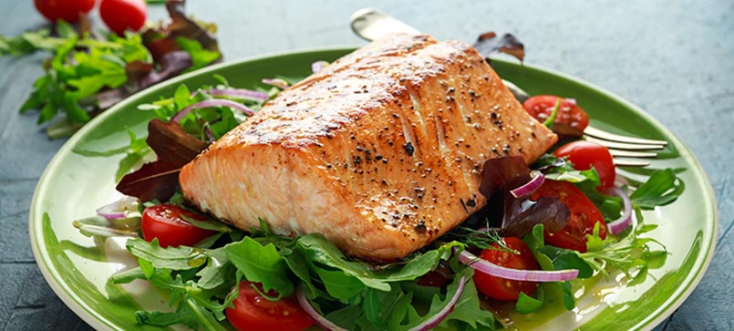 A cooked salmon filet on top of a fresh super greens salad