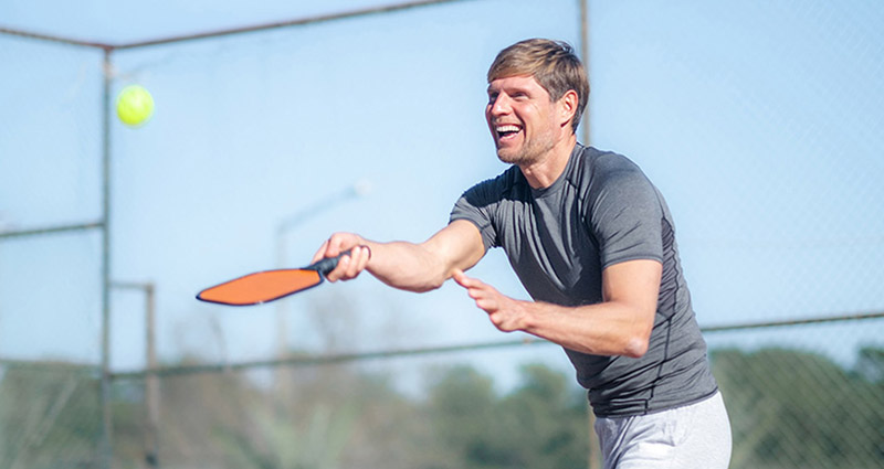 A man smiling while swinging a pickle ball paddle