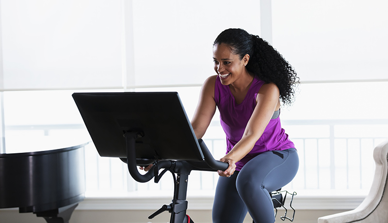 A mid adult African-American woman in her 30s exercising at home in the living room, on an exercise bike.