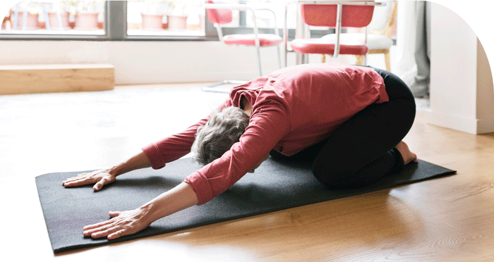 An older woman stretching her back on a yoga mat indoors