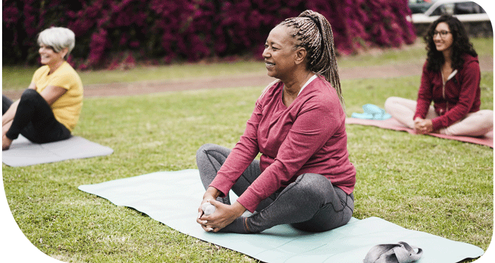 3 women doing a butterfly stretch on yoga mats outdoors