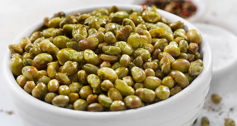 A bowl filled with green and brown edamame seeds placed on a light surface.