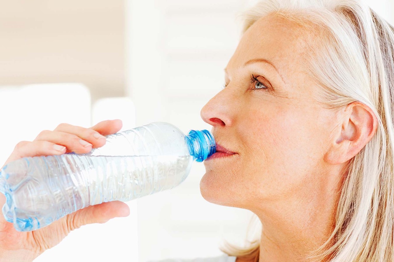 Older woman drinking water from a plastic bottle.