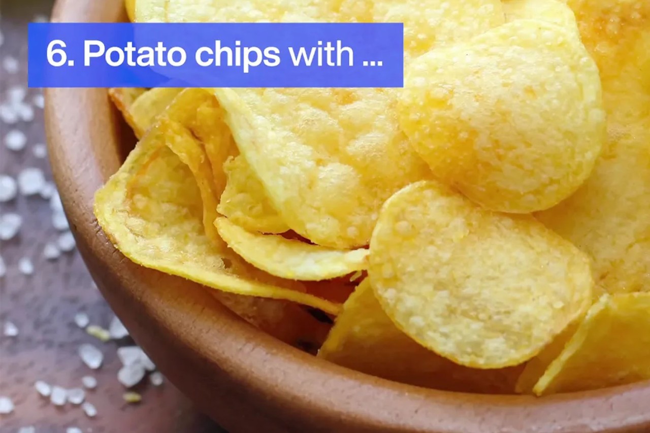 Close-up of potato chips in a wooden bowl with salt sprinkled nearby.