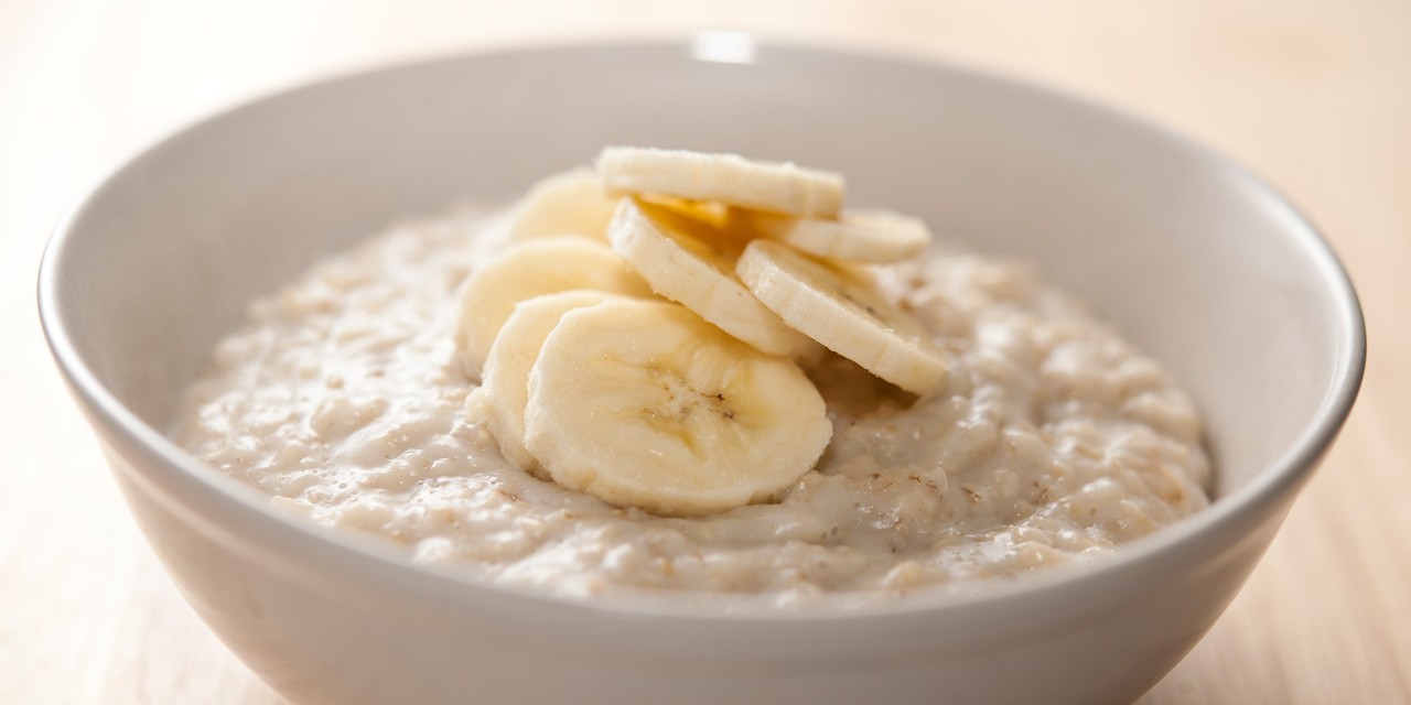 Bowl of oatmeal topped with banana slices on a wooden surface.