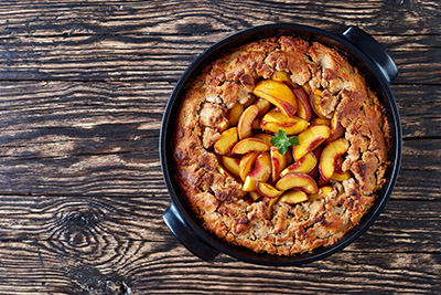 Homemade Peach Cobbler with crisp topping in a black dish, made from fresh summer peaches, horizontal view from above, flat lay