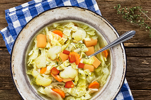 Fresh homemade vegan cabbage soup with carrot and potato, sprinkled with thyme and served in rustic soup plate, photographed overhead