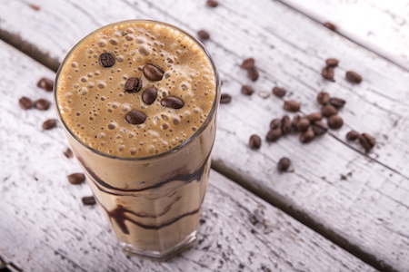 Cold chocolate milkshake frappe in tall glass with ice on white wood background