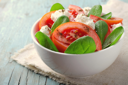 Tomato salad with spinach, cottage cheese, olive oil and pepper on blue wooden background, toned