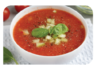 A white bowl of red tomato soup, topped with diced cucumber and a sprig of basil, on a textured napkin.