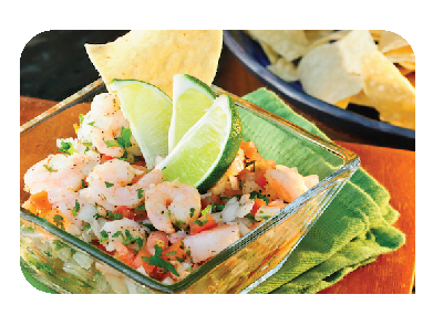 Glass bowl of shrimp ceviche with lime wedges and tortilla chips on a green napkin.
