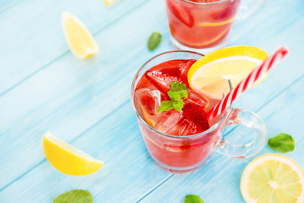 Colorful refreshing drinks for summer, cold strawberry lemonade juice with ice cubes in the glasses garnished with sliced fresh lemons