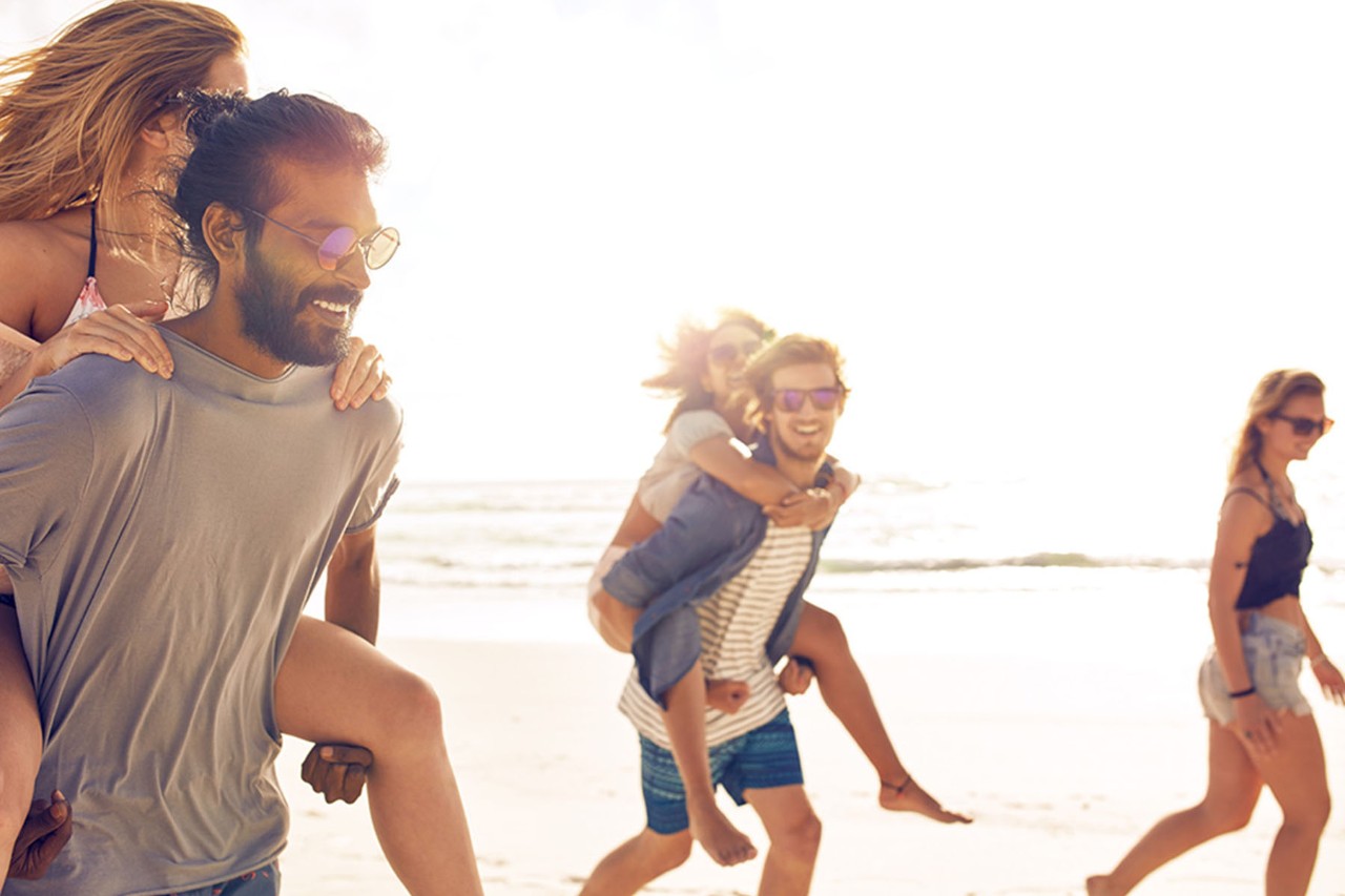 Friends having fun on the beach, giving piggyback rides.