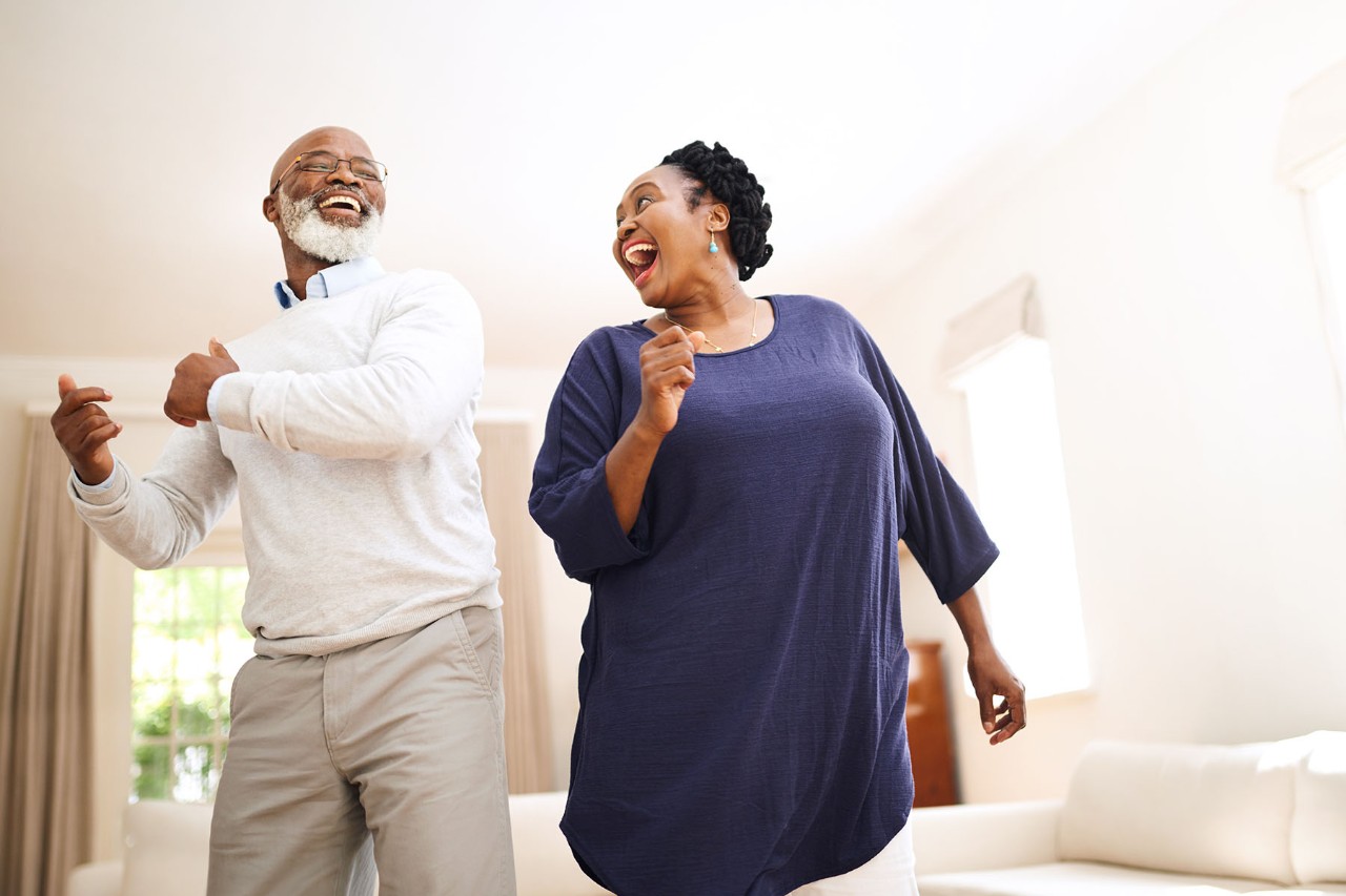 Happy older couple dancing together in a bright living room.