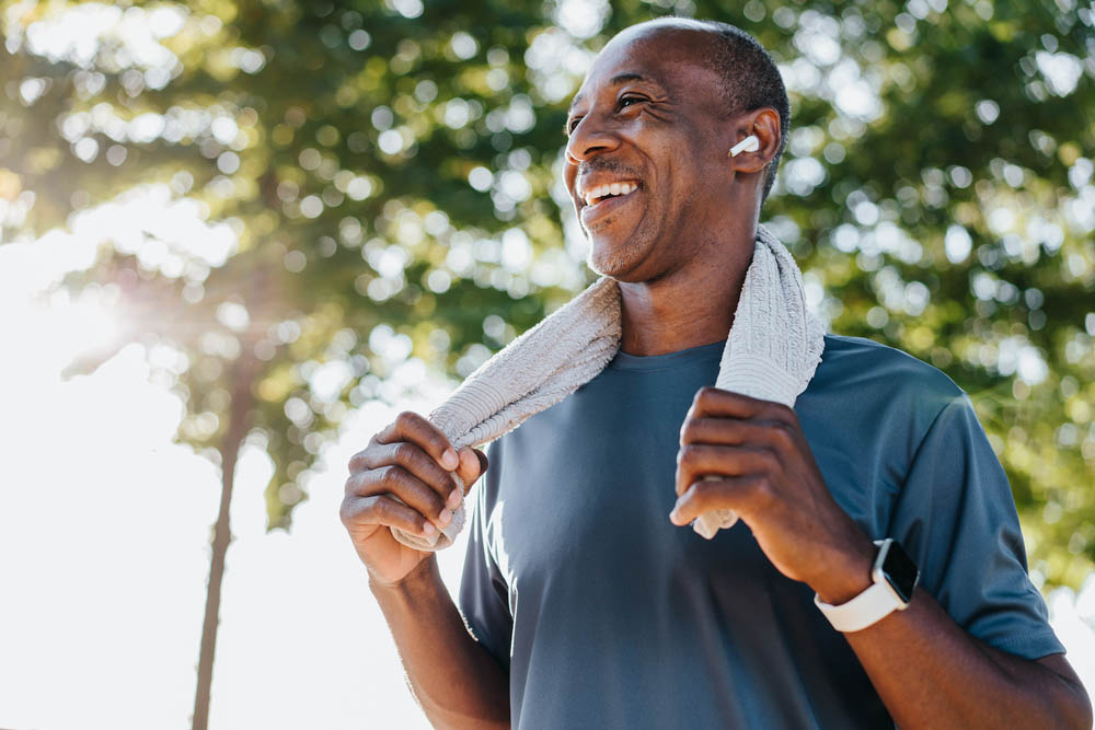 Smiling man with a towel around his neck after a workout outdoors.