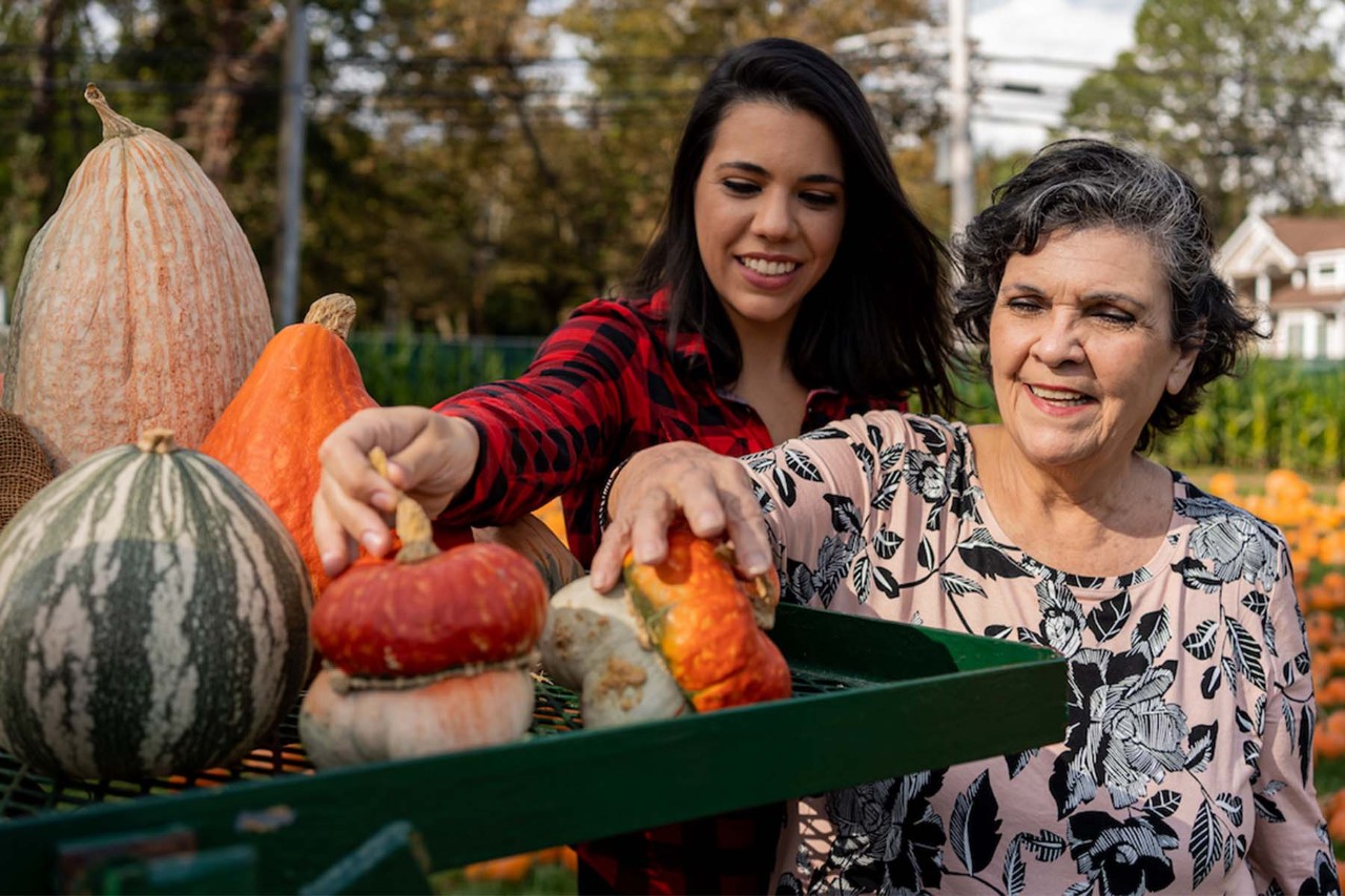 Smiling older woman and younger woman selecting pumpkins at an outdoor market.