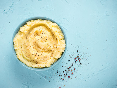 Mashed potatoes with peppers in blue bowl on blue concrete background. Top view or flat lay. Copy space.
