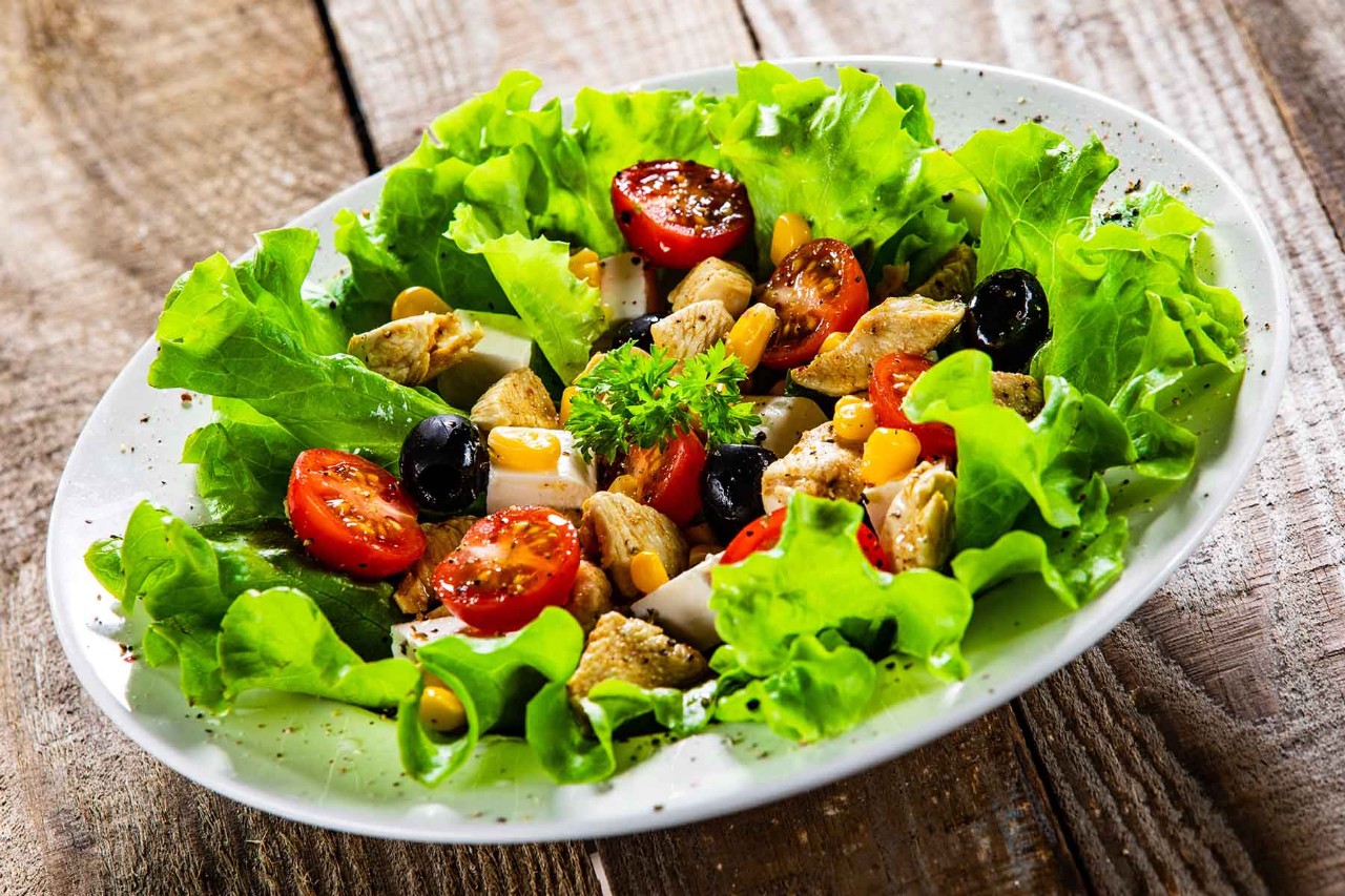 Fresh salad with lettuce, cherry tomatoes, olives, corn, and chicken on a white plate