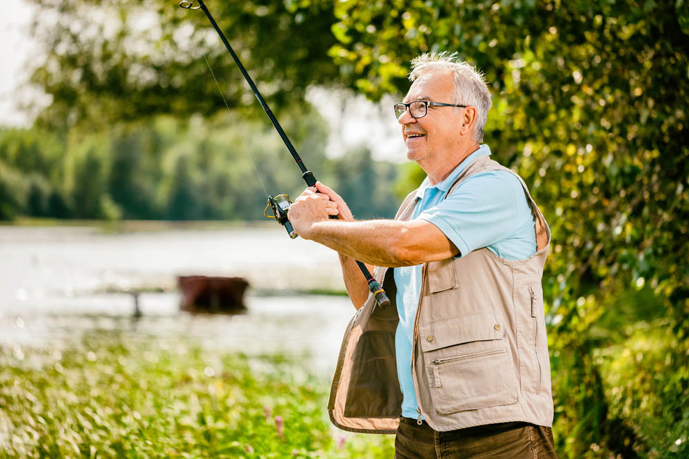 Happy senior man is fishing on sunny day. 