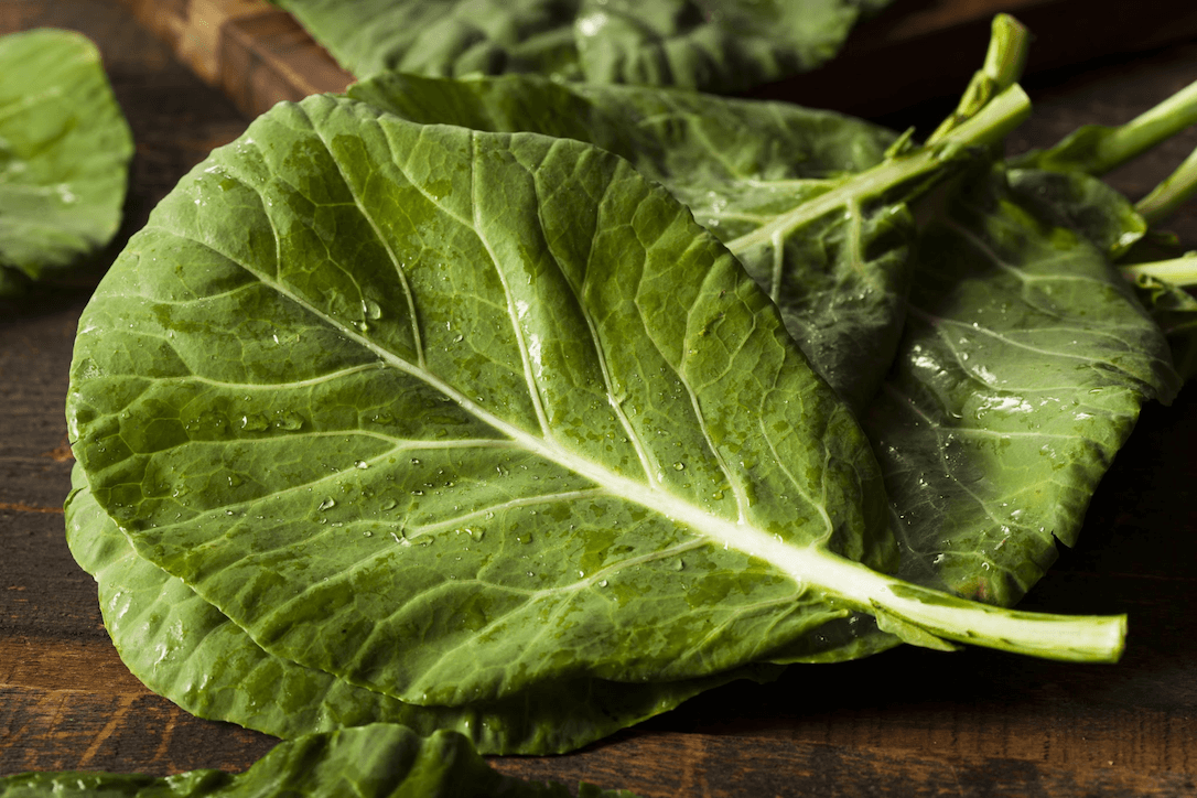 Fresh collard greens with water droplets on a wooden surface.