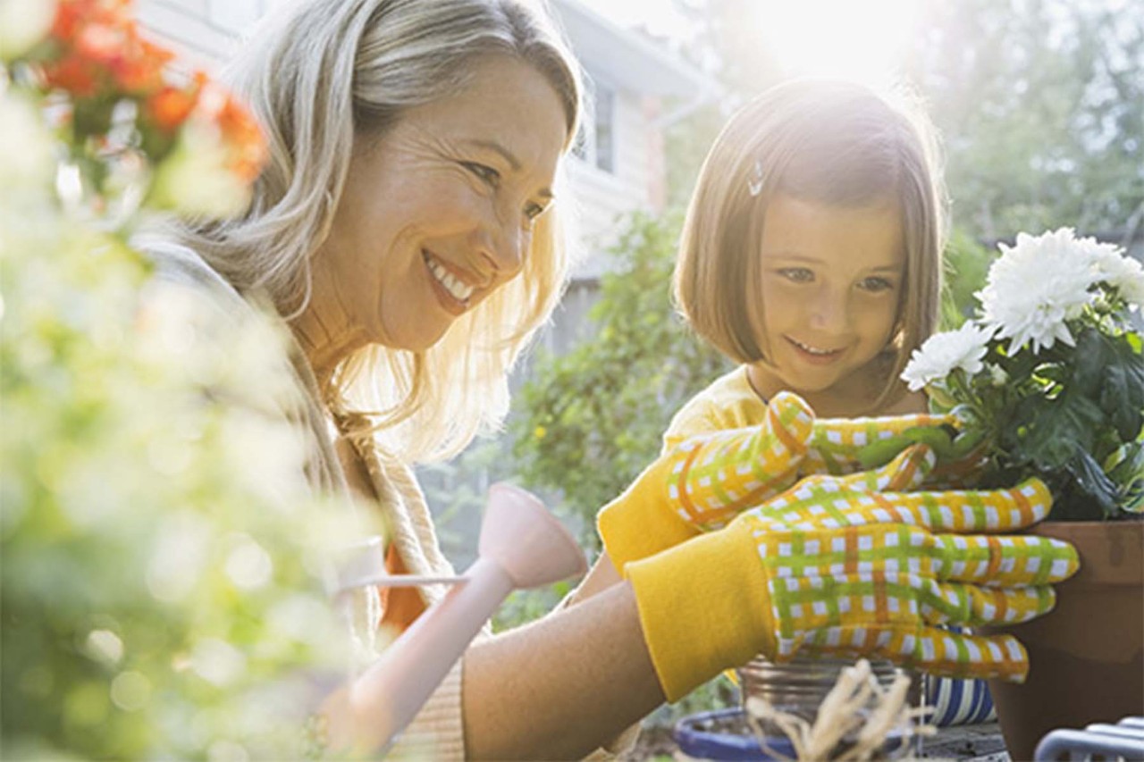 Woman and young girl gardening together, smiling and planting flowers.