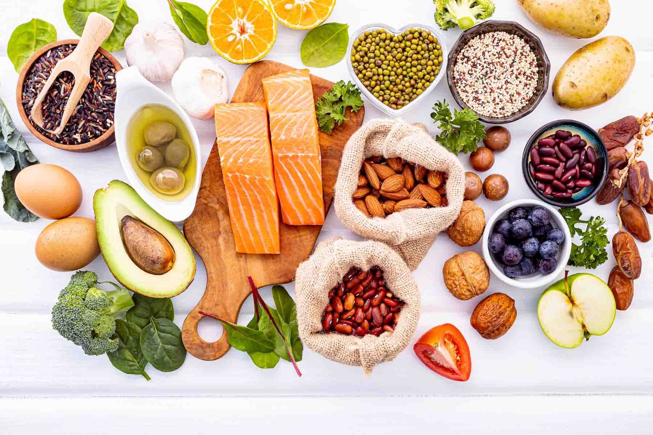 Top-down view of healthy foods including salmon, avocado, eggs, nuts, berries, and vegetables arranged on a white background.