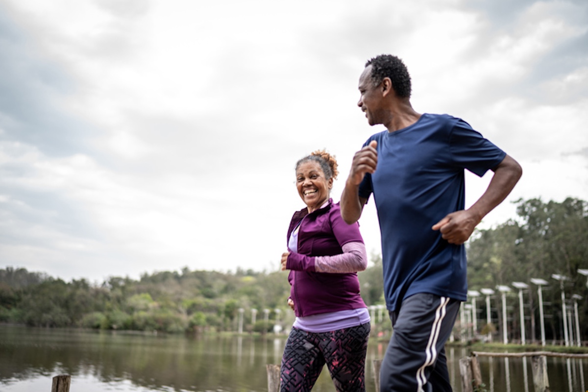 A man and a woman jogging together along a scenic path by a lake, smiling and enjoying their exercise in an outdoor setting.