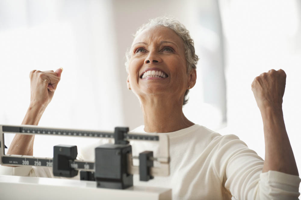 Person celebrating while standing on a mechanical scale, smiling with arms raised in triumph.