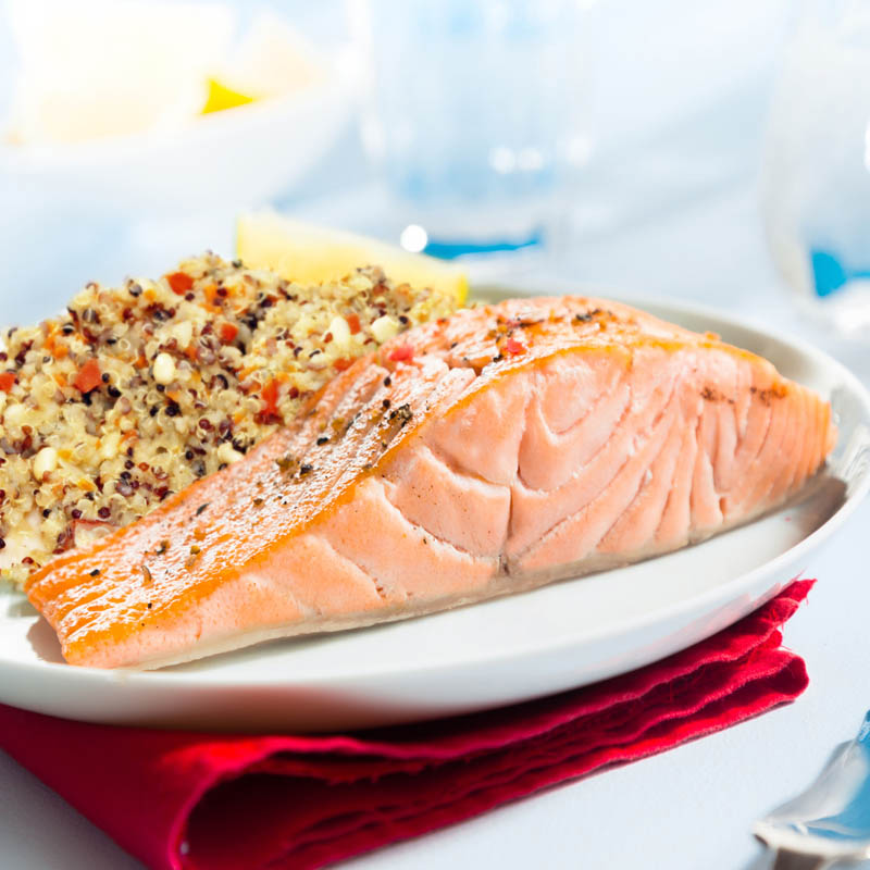 Healthy gourmet pink salmon steak rich in omega-3 served with fresh green mangetout peas and lemon, close up showing the texture of the fish