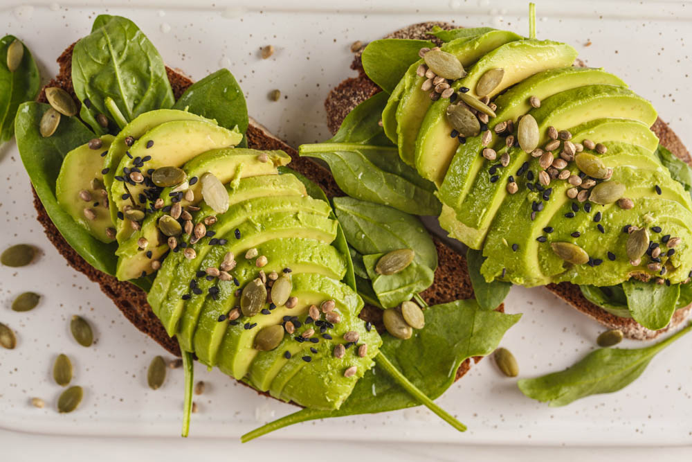 Two slices of toast topped with avocado, spinach, and seeds, arranged on a plate.