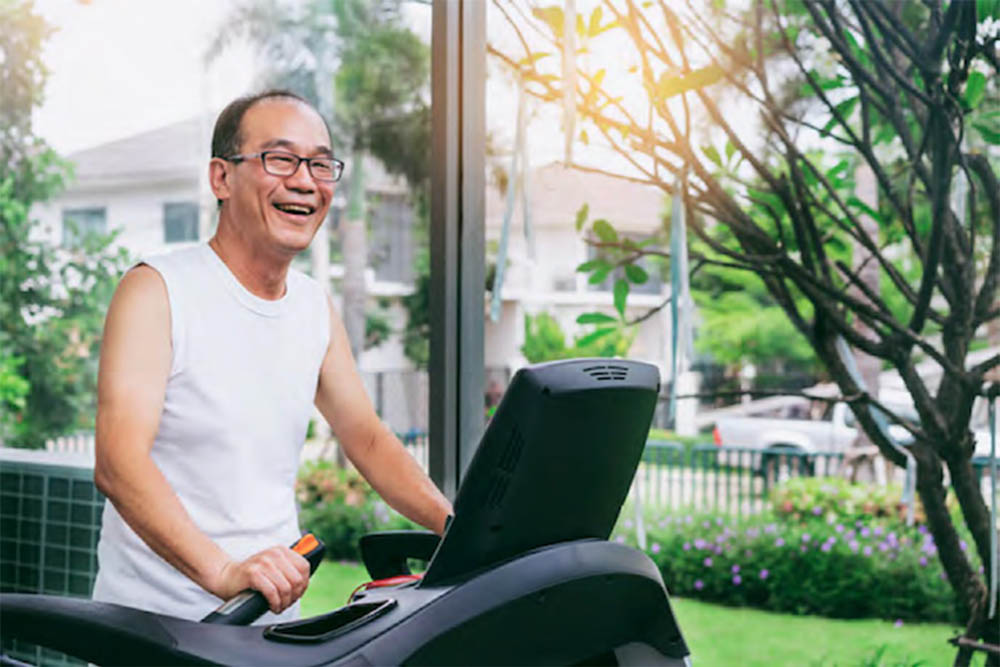 A smiling older man exercising on a treadmill in a bright, green indoor setting.